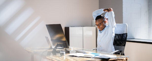 Person seated at a desk, gently stretching arms overhead in a calm workspace